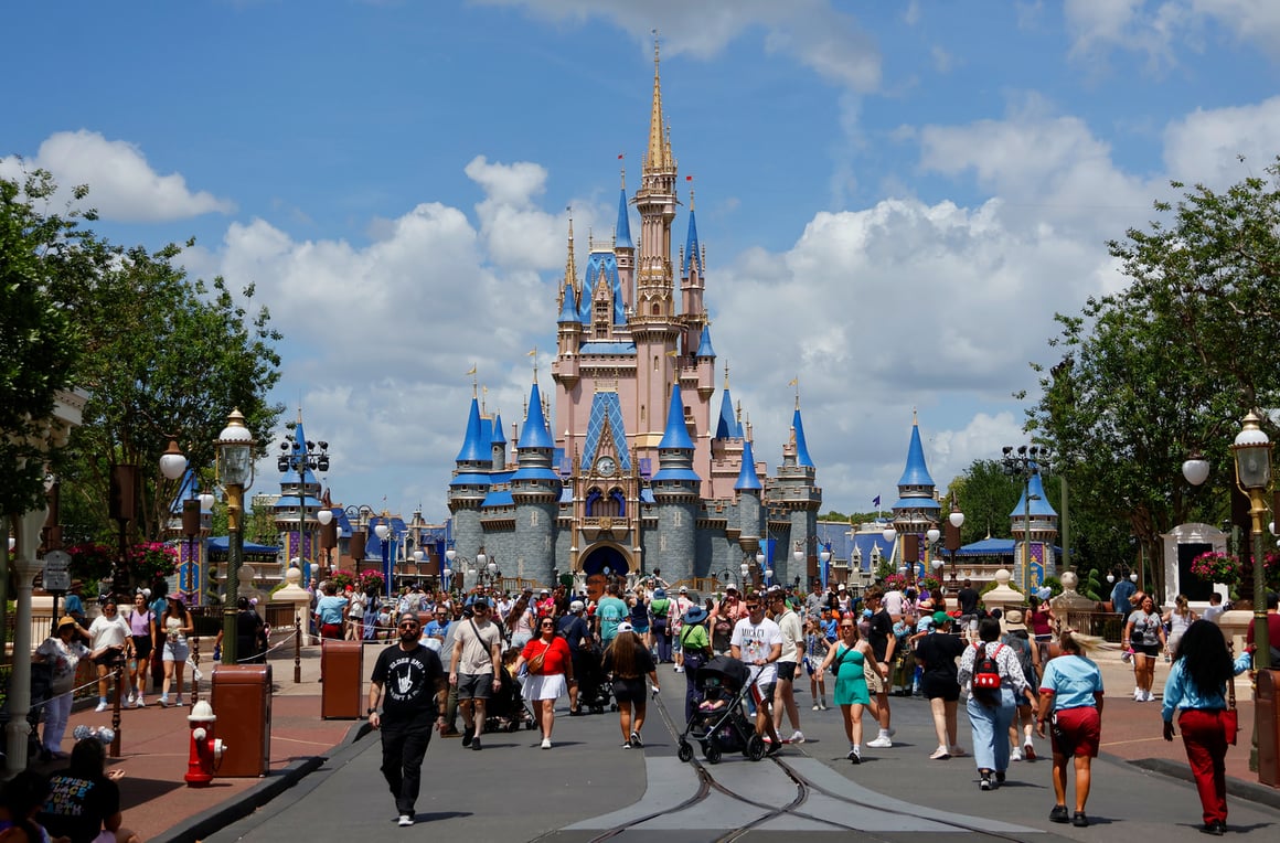A crowded street leading to Cinderella Castle at Walt Disney World's Magic Kingdom, featuring two brown trash cans placed close together.