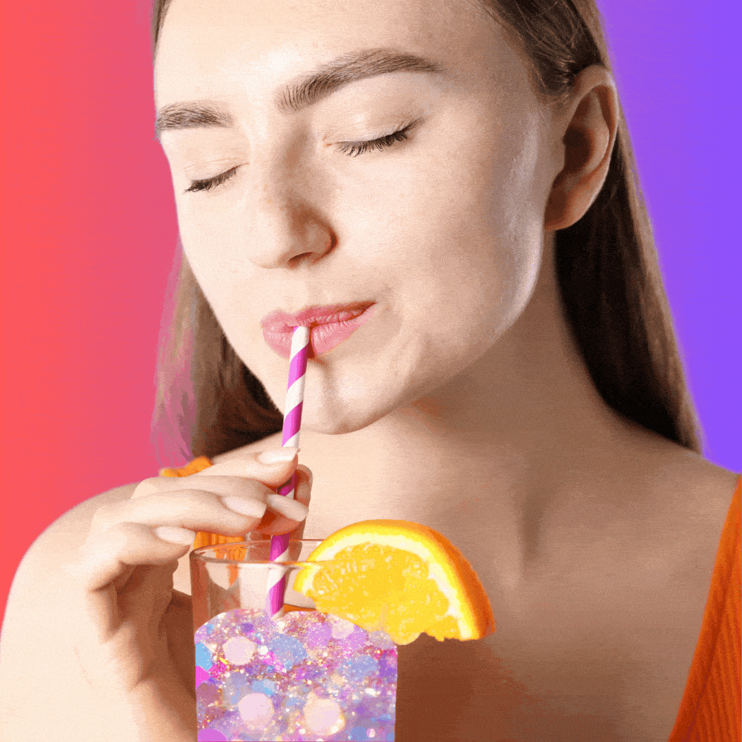 A woman using a straw to sip from a pint glass full of sparkles. 